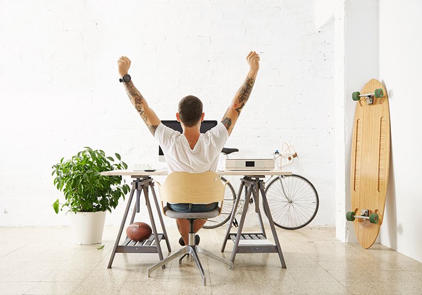 tattooed-lucky-freelancer-front-his-working-space-surrounded-with-his-hobby-toys-longboard-vintage-bicycle-green-plant-stretching-his-hand-air-while-making-break